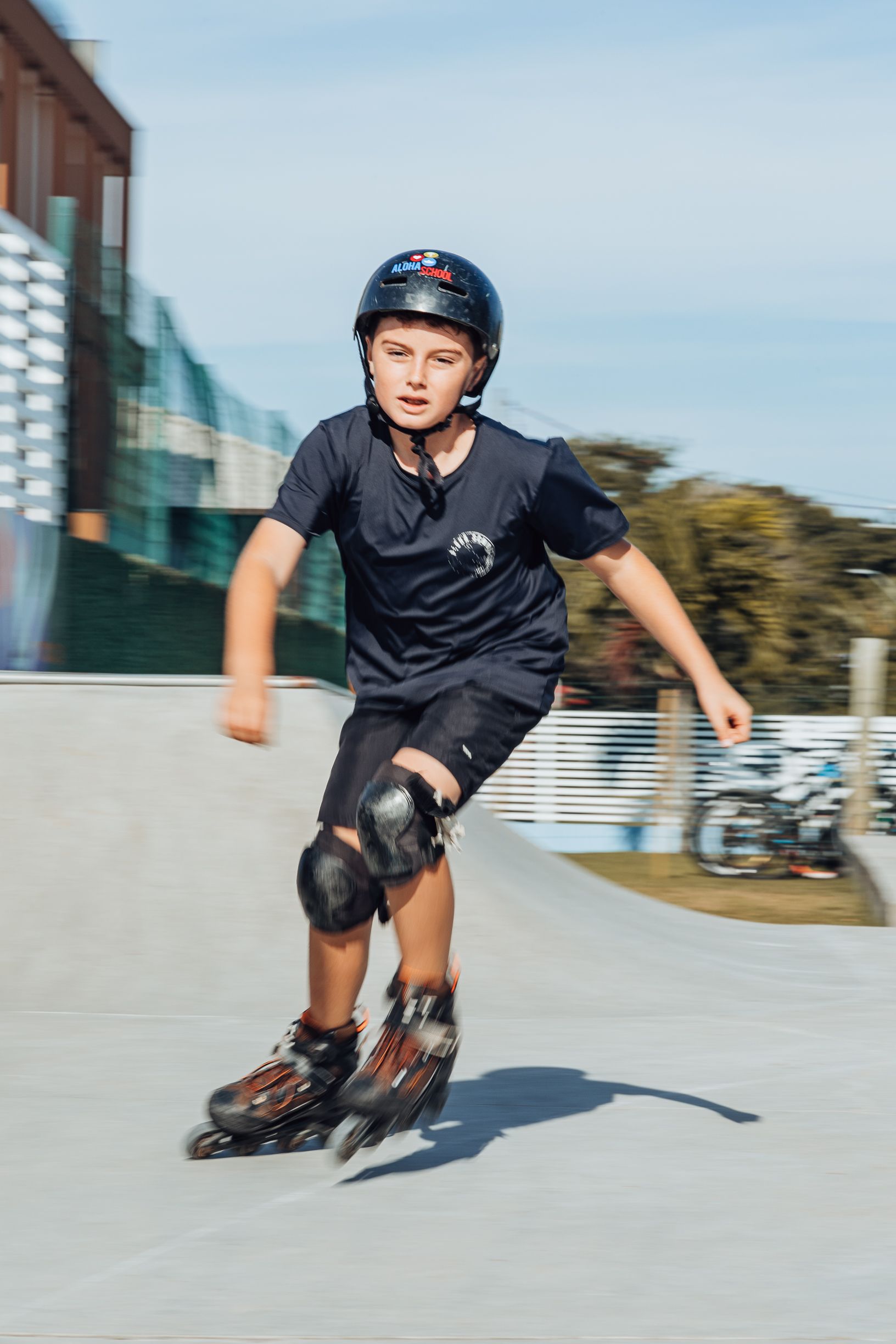 Aluno da Aloha de capacete e joelheiras andando de patins em uma área externa.